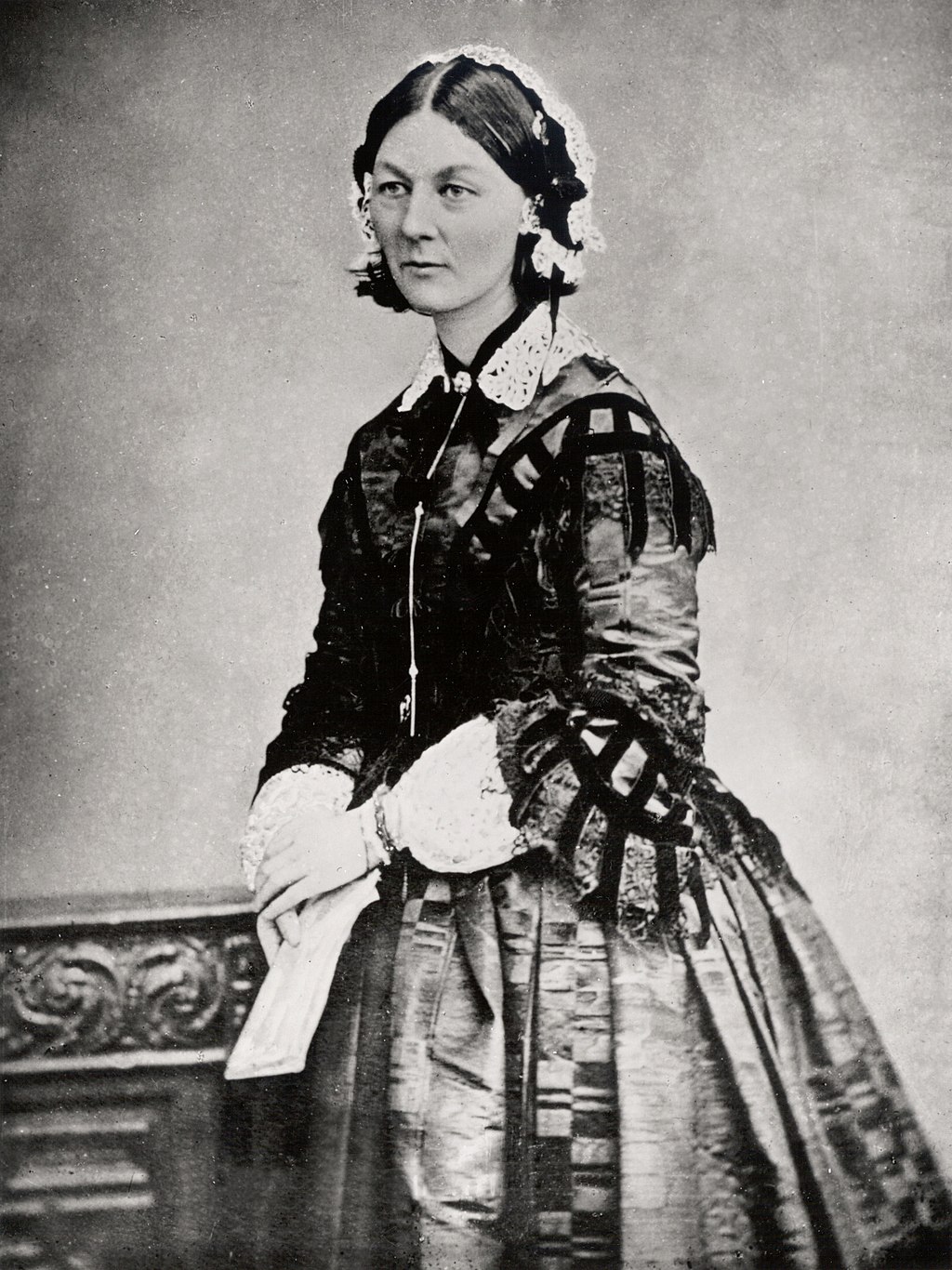 Three quarter portrait of Florence.  she is wearing a lace cap and shirt with a fitted jacket over the top.  She is holding a folded piece of paper in her hands and wears a wide skirt.