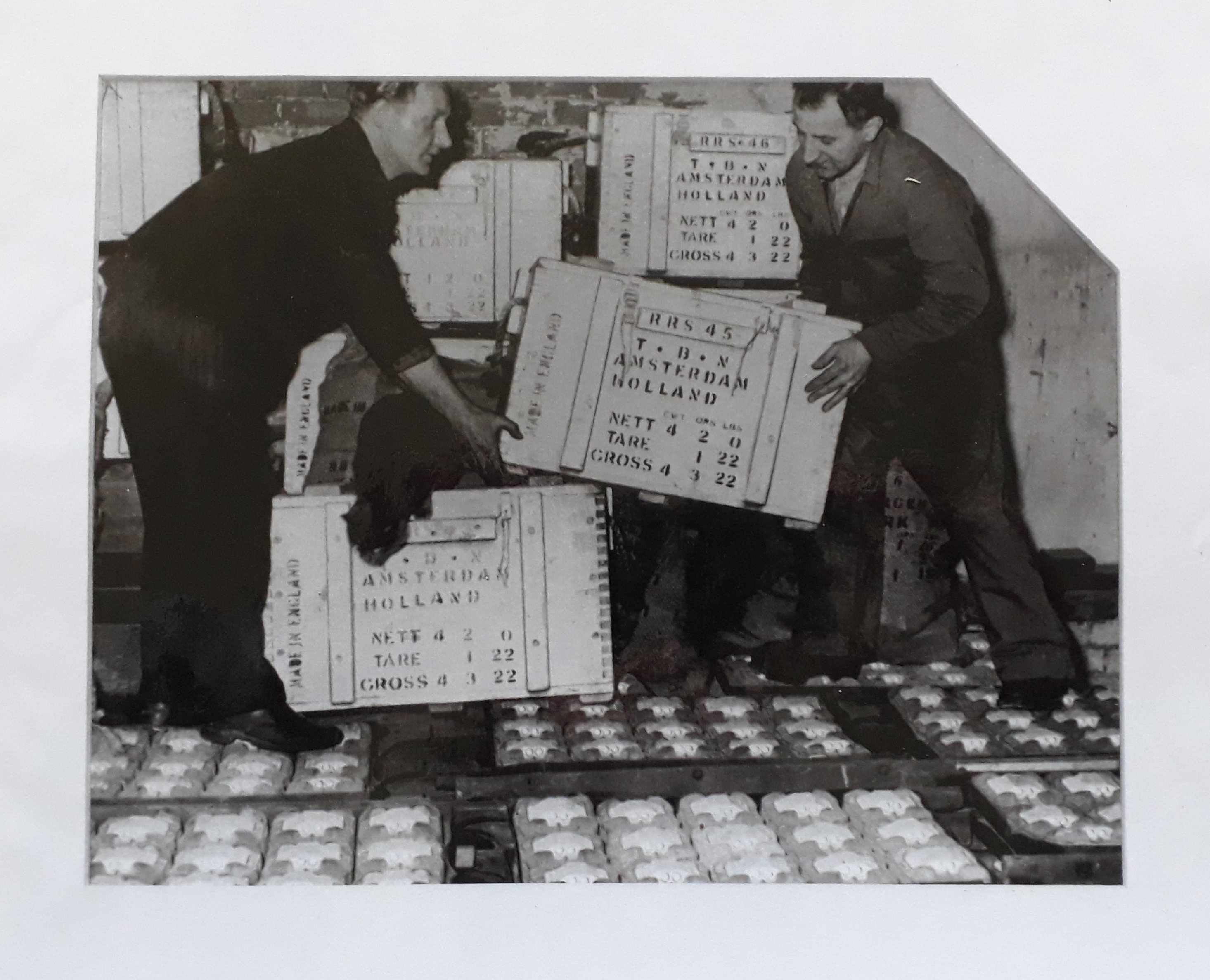 Black and white photograph showing two men moving wooden crates of catseyes