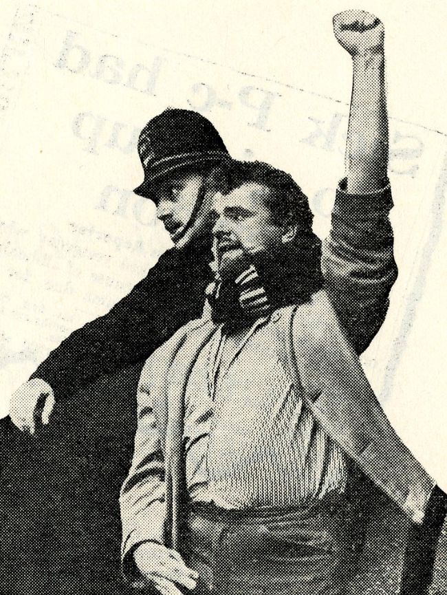 Photograph of policeman with his arm around a protester as he is shouting with his hand in the air