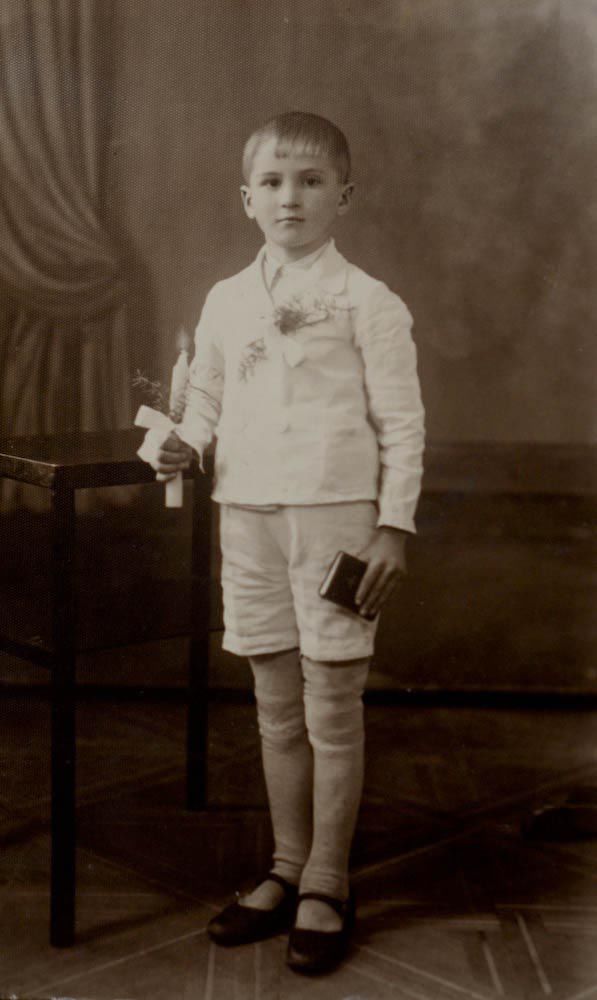 Young Polish boy Edward in his First Communion clothes in 1943.  He wears all white suit and holds a bible and a candle