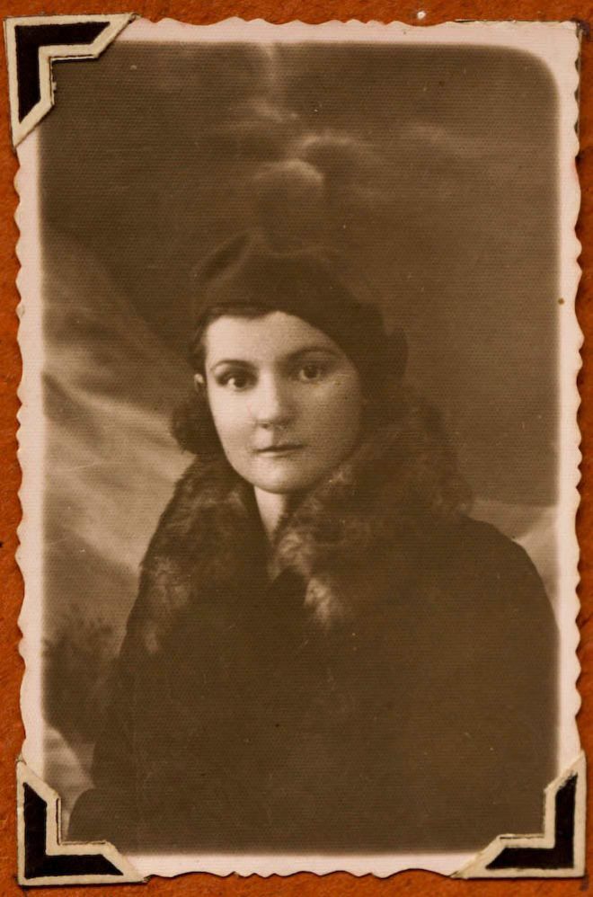 Lola wears a fur collar and beret type hat.  She has dark, shoulder length hair and is looking straight at the camera.