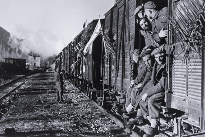 A group of soldiers sitting and standing by an open doorway on a train.