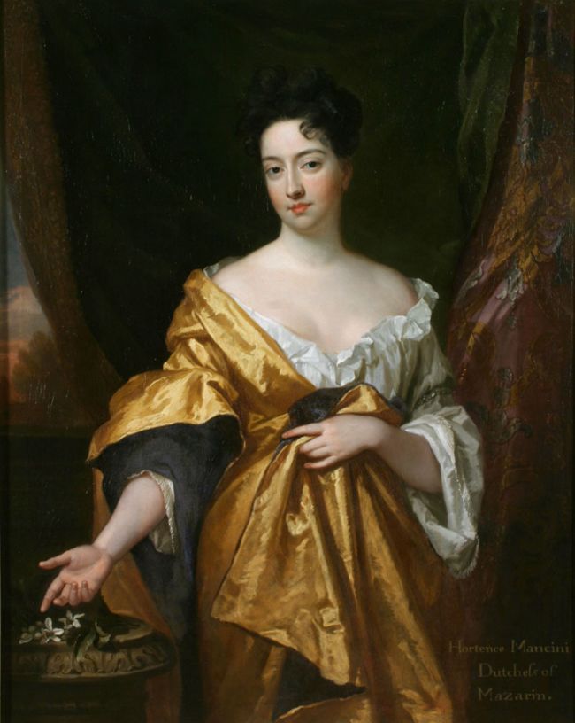 The Duchess of Mazarin by Sir Godfrey Kneller. Portrait of the top half of the Duchess facing towards the artist wearing a gold dress and white under-gown, holding one arm out towards some small white flowers.