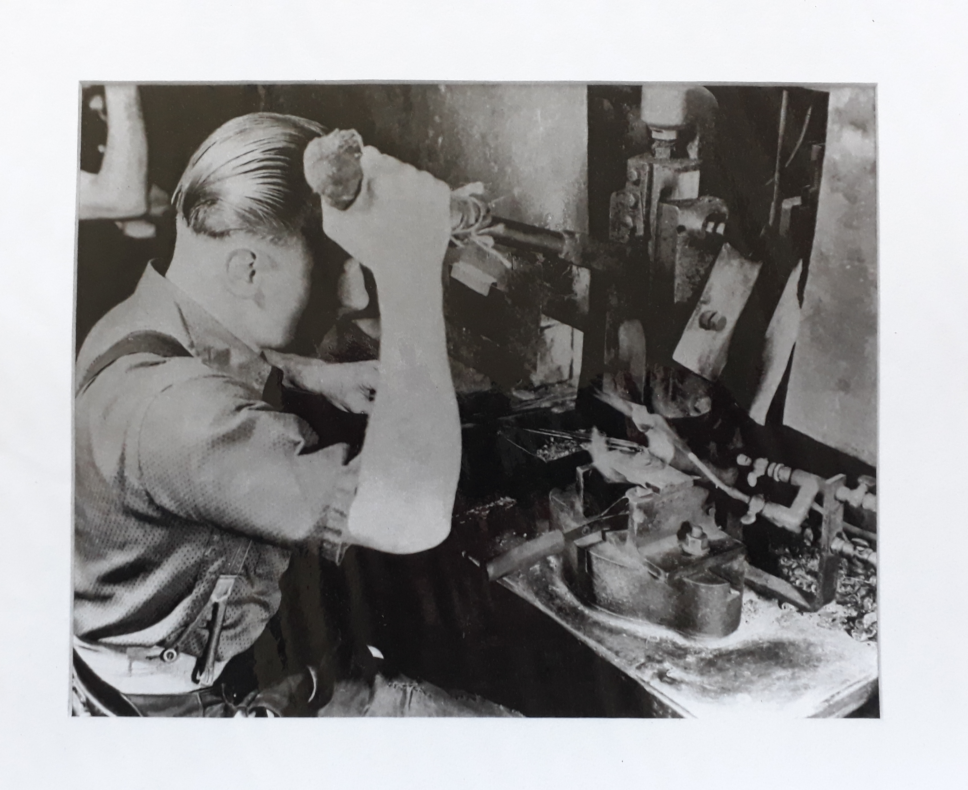 Black and white photograph showing a man operating a machine. He is pulling down on a lever