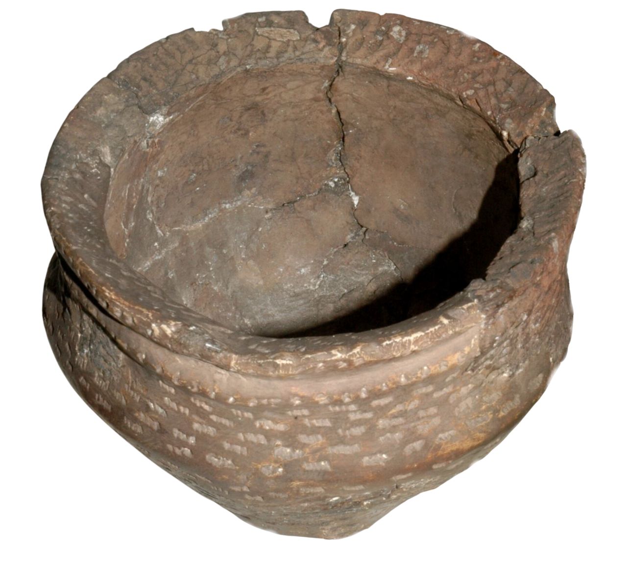 A weathered, ancient pottery bowl with a rough, cracked surface. The bowl is rounded with a wide opening and has visible horizontal ridges around its body. The rim is slightly uneven and chipped, showing signs of age and wear. The overall colour is a muted brown.