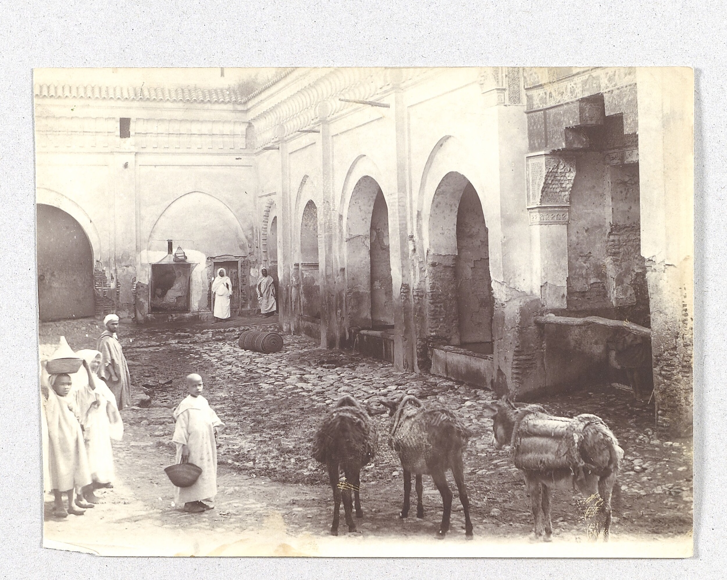 Black and white photograph showing adults and children in jalabiya with donkeys in the foreground.