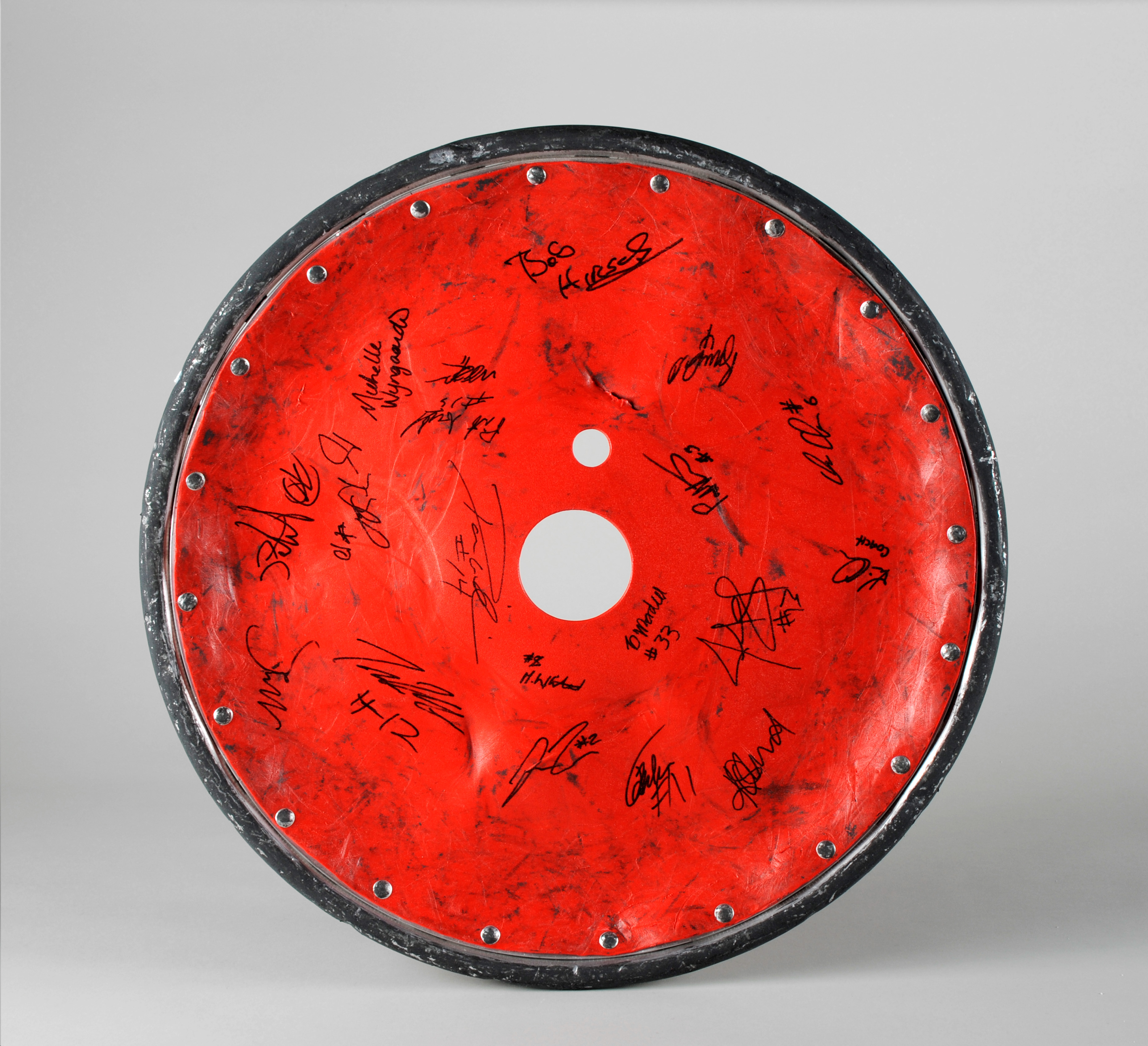 Colour photograph of a wheel, with a red plastic guard. The guard is covered in dents and is ripped.