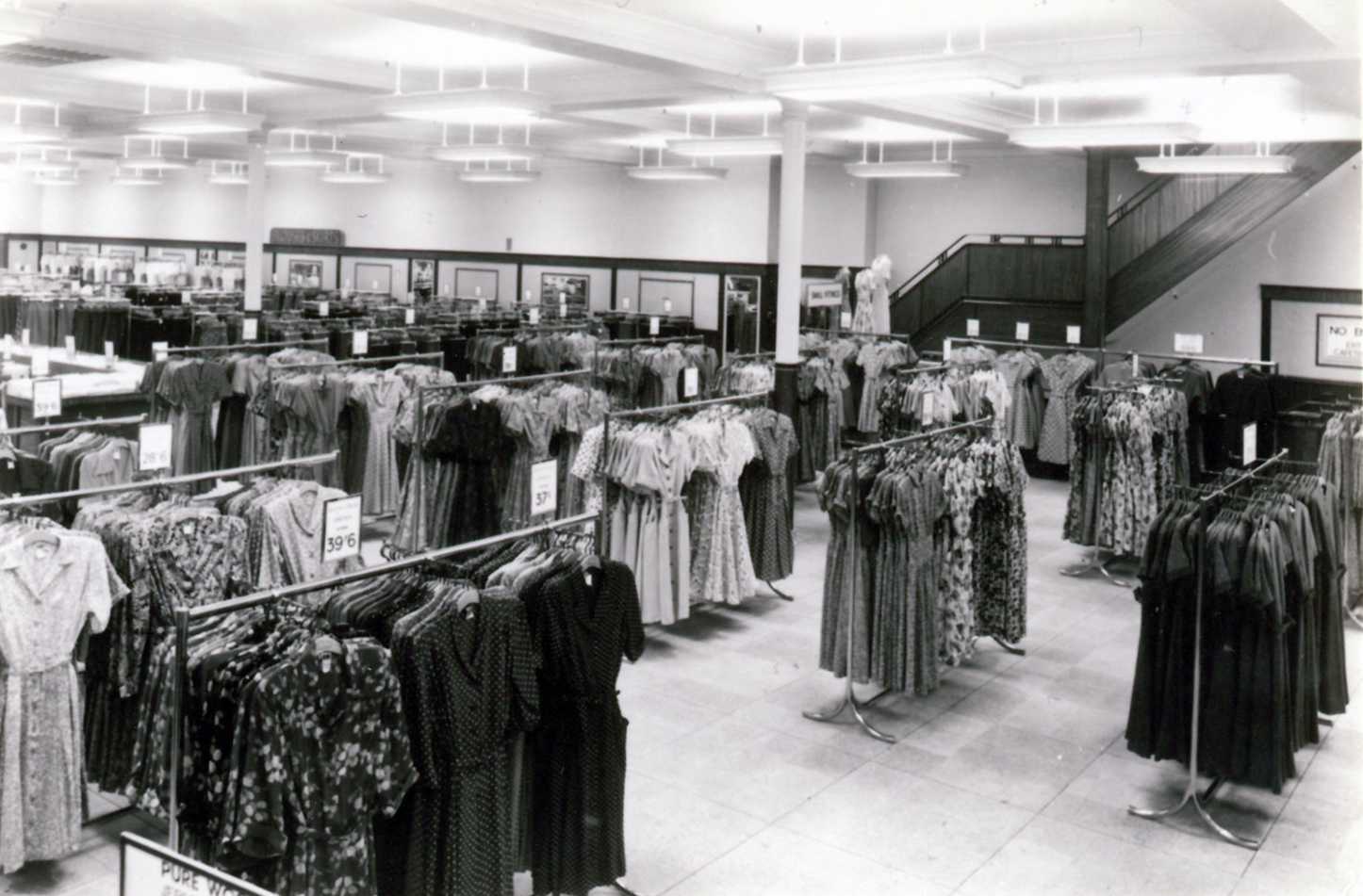 Black and white interior of a Marks & Spencer clothing department with rows of dresses on racks.