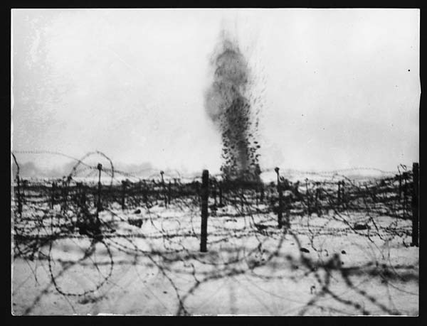 Shell exploding at The Front, France during the First World War. It can be seen in the distance, through rows of barbed wire stretching across no-man's-land.