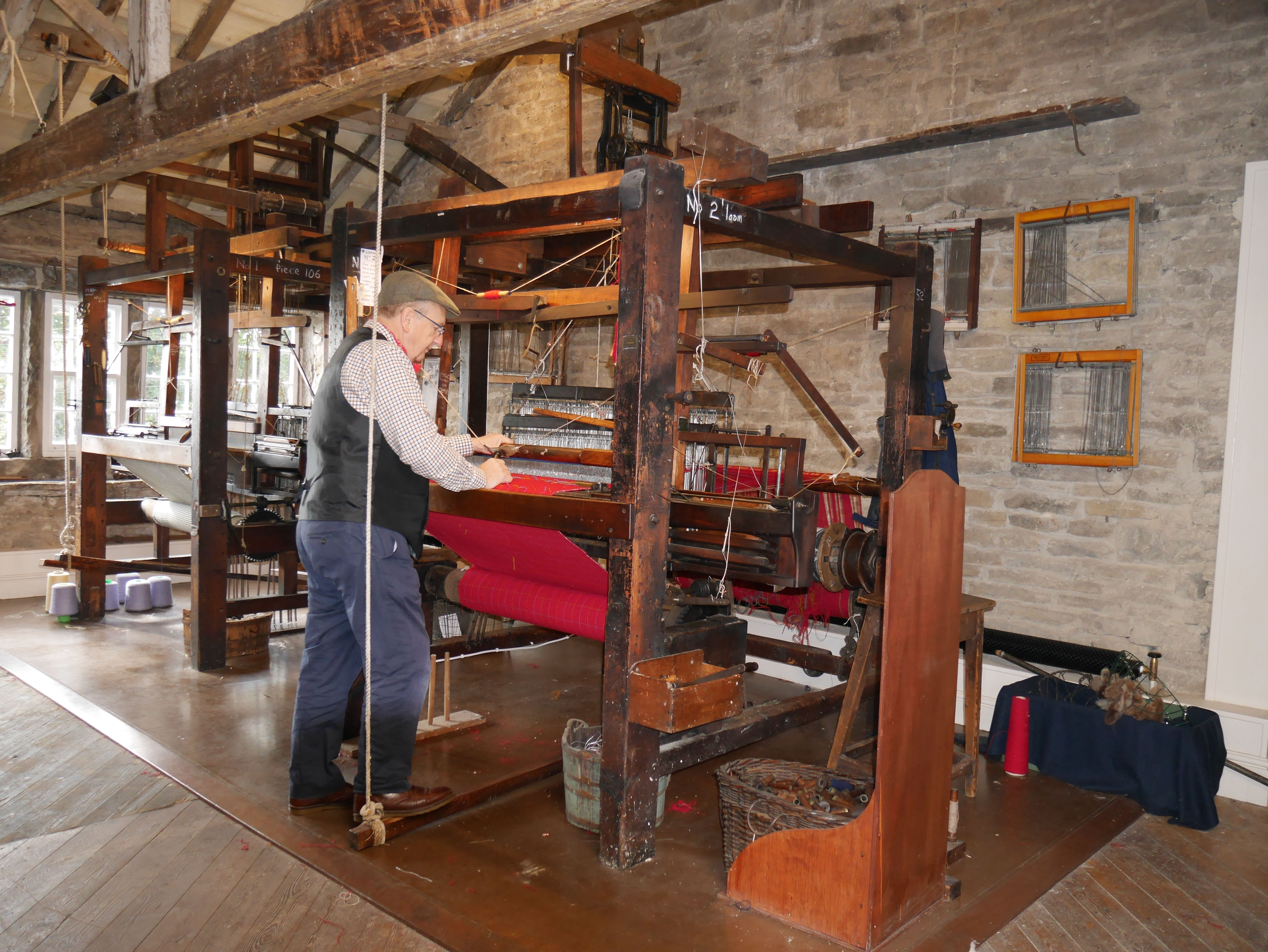Large wooden loom with red cloth being woven on it.
