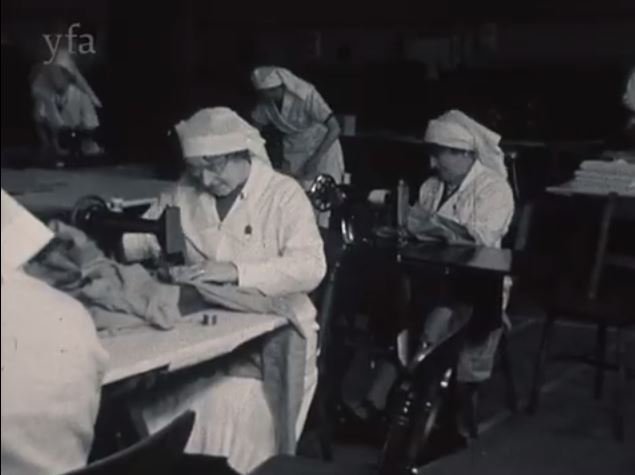 Film still showing women in white uniforms sewing