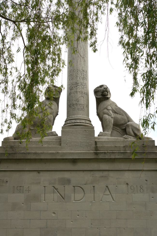 Two stone lions sit, one either side of a column which has engravings in both English and Hindi