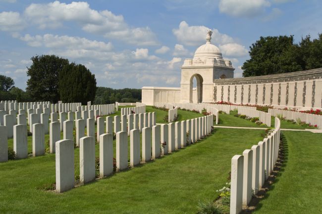 Rows of simple, plain white grave markers in grassed area with a wall around.