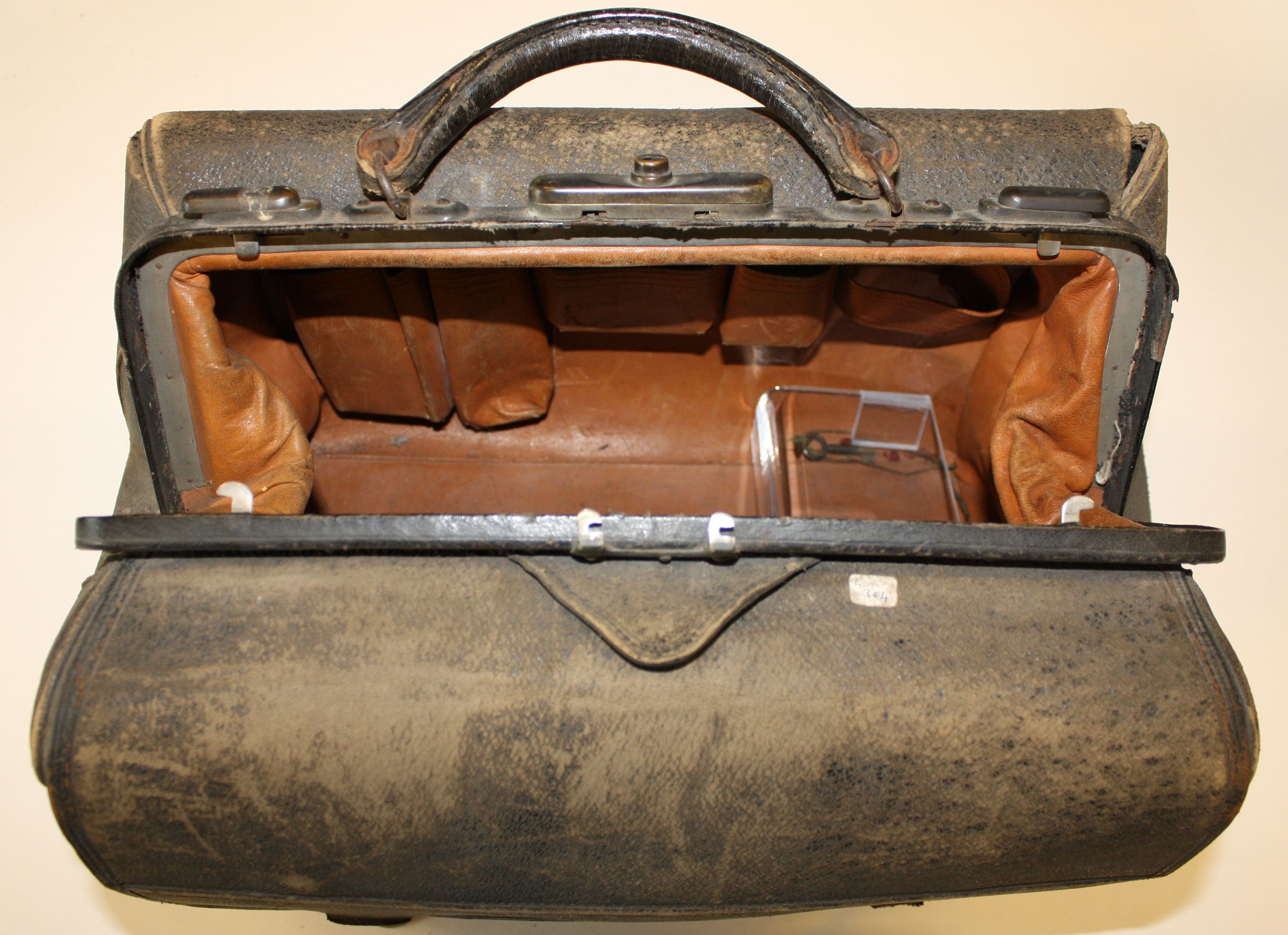 Open vintage leather doctor's bag with a worn, dark exterior and brown leather interior. The bag's compartments and metal clasps are visible.