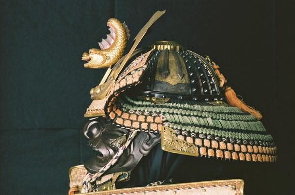 Samurai Helmet and Face Mask showing a golden fish like creature on the front and highly decorated sides.
