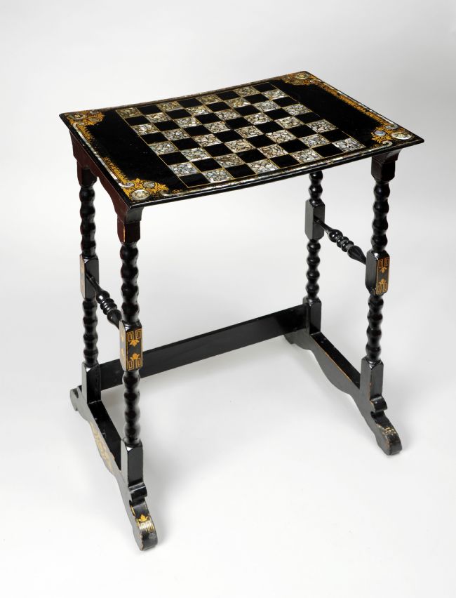 A papier mâché table decorated with gilt and mother of pearl shell around the top edge. The chess board design is inlaid mother of pearl.
