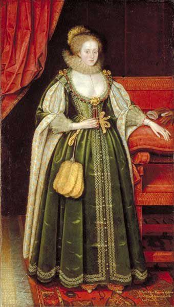Full portrait of a lady with a pale face and hair pulled back.  She is wearing an expensive green dress and is standing next to a deocrated red chair.