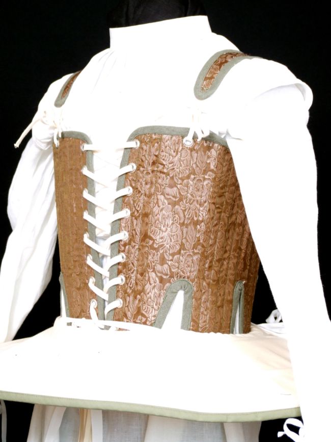 white shift with a brown corset over the top and laced at the front.  Round the waist, a wide strip of fabric sticks out straight all around the body