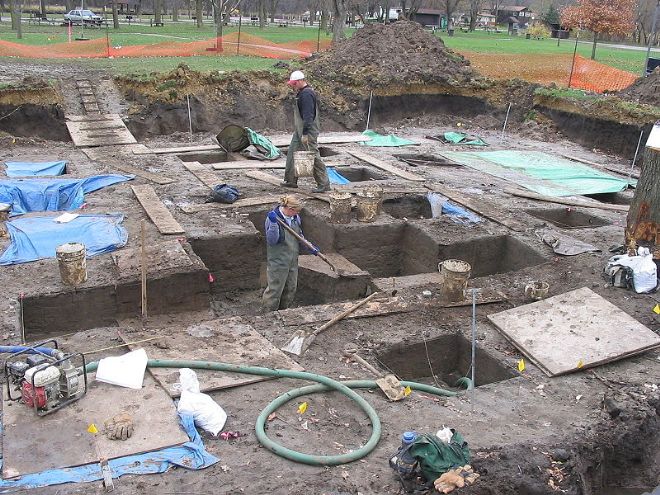 Photo of Archaeologists digging down in a field into the mud, looking for artefacts