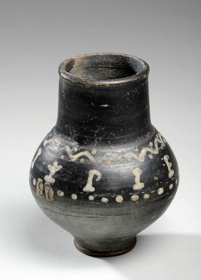 Black beaker that expands out in the middle.  It is black with a white design of wavey lines and dots.