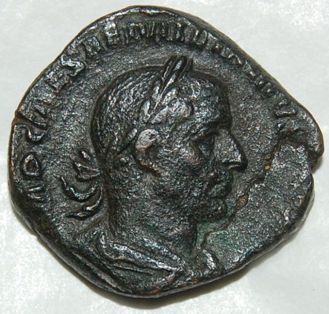 An old Metal Roman coin, Showing the Head of Caesar with an inscription around the outside.  The coin is very mis-shapen and more square than round.