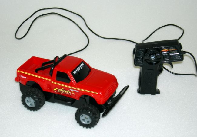 The truck is red with chunky black wheels and is connected to the controller by a wire.