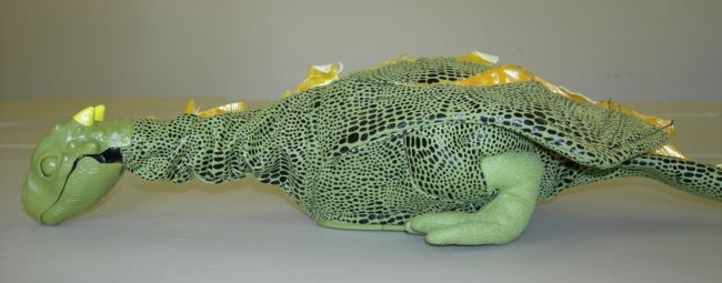 Norbert the dragon has his head on the floor and his eyes closed.  He is green with dark scales and a yellow trim to his wings.