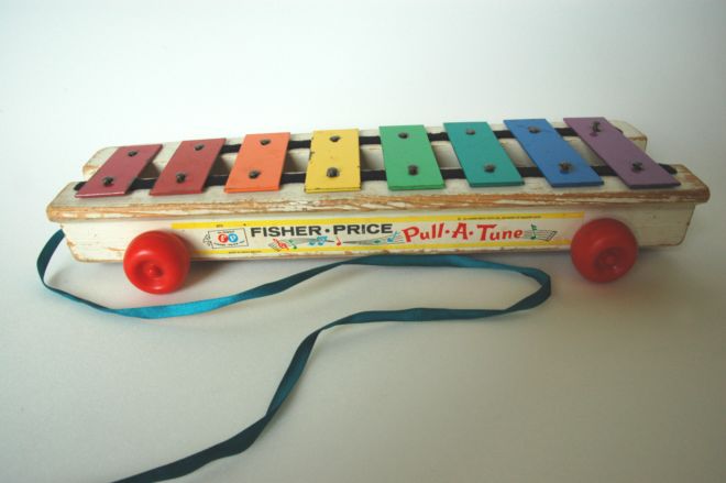 1950s pull-along xylophone toy by Fisher Price.  It has 8 bars which are all painted different colours of the rainbow and rolls on red plastic wheels.