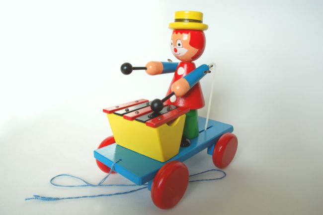 Wooden Pull-along Clown Playing Xylophone.  The clown has a beater in each hand to hit the xylophone with.  He has orange hair and wears a yellow hat.