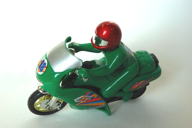 A new clockwork motorcycle toy.  The bike and rider are coloured green adn made of plastic.  The rider wears a red helmet.