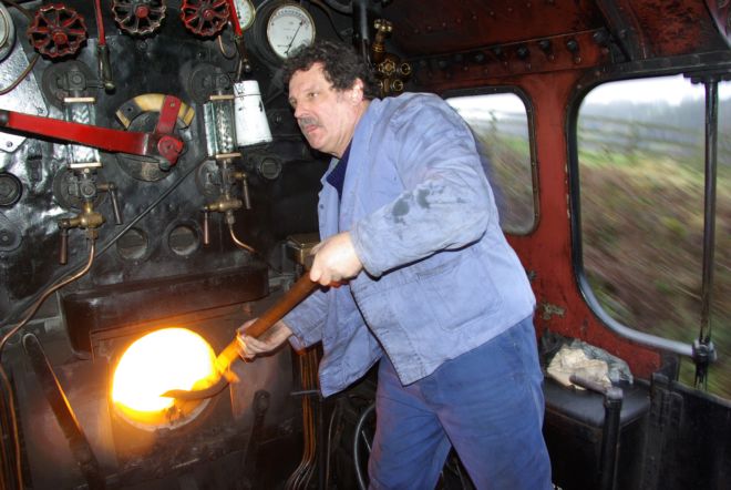 Steam train fireman feeding the fire with a shovelfull of coal