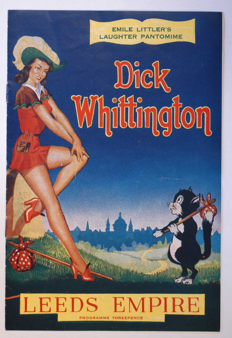 Colour programme showing a female Dick Whittington wearing a short red dress and heeled shoes with a cat. In the background in a winding road leading to  a city
