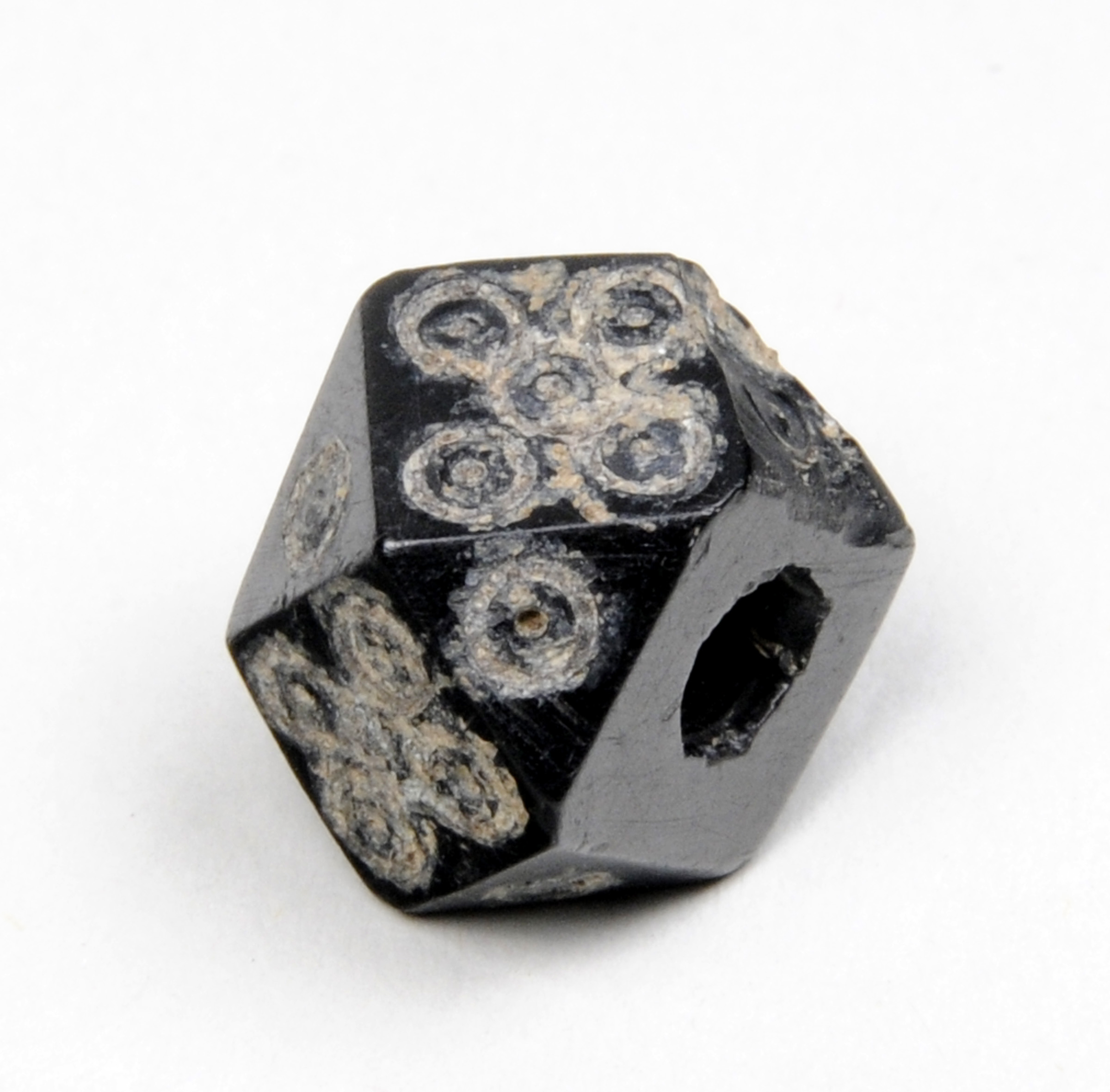 Colour photograph of a jet black bead and the curly engravings on it