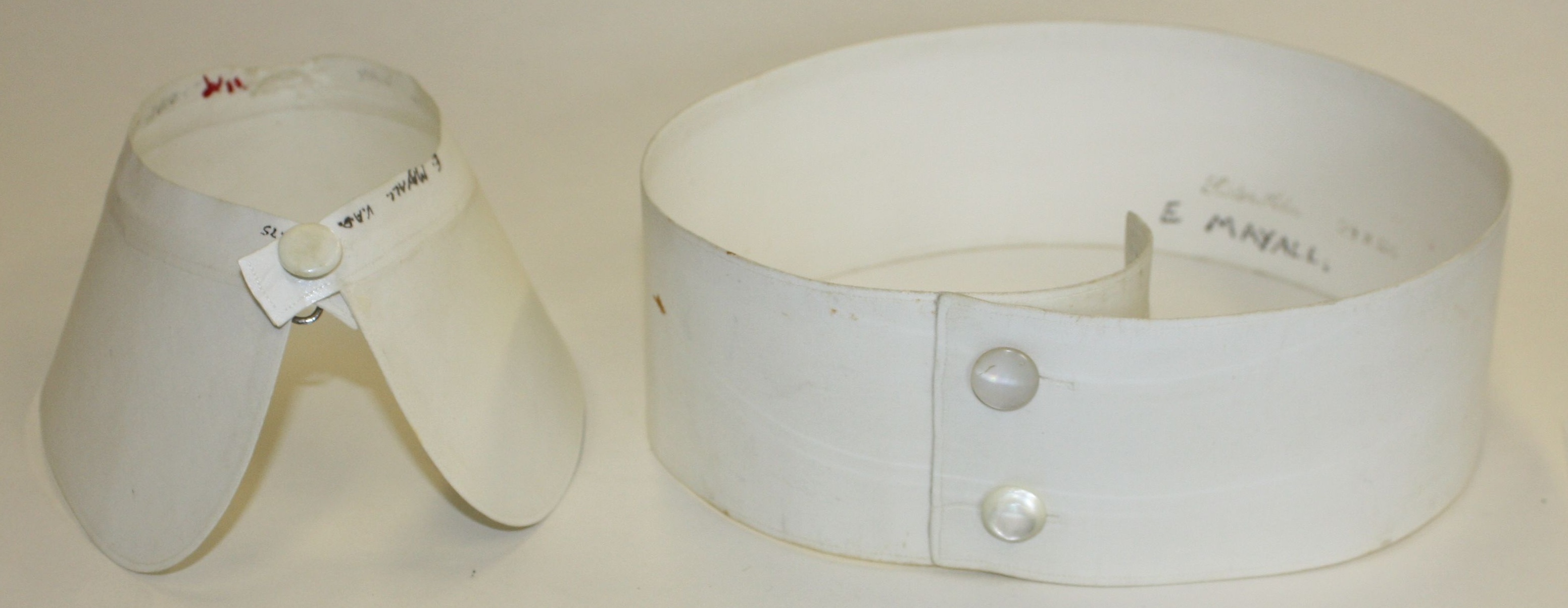 A white detachable cuff and belt are displayed against a neutral background. One is a winged cuff, standing upright, while the belt is straight with buttons.