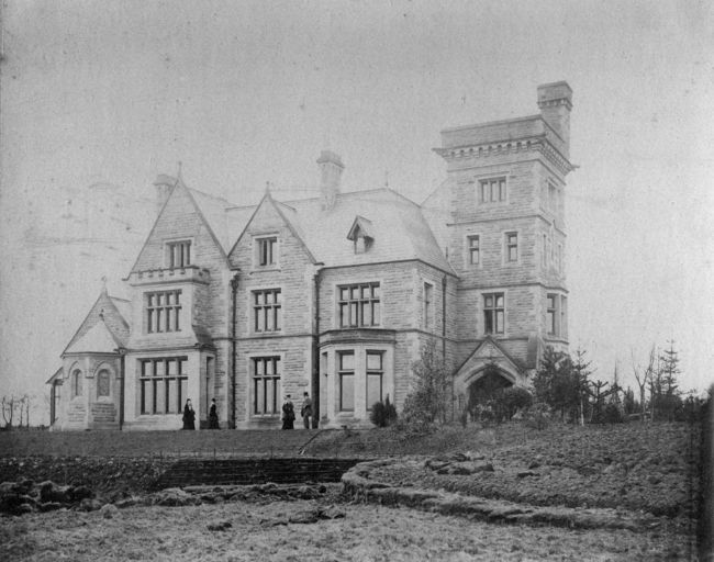Black and white photograph of the exterior of Singleton Hall, Preston.  It shows a large, grand house with a square tower on one end.  Four people standing outside.
