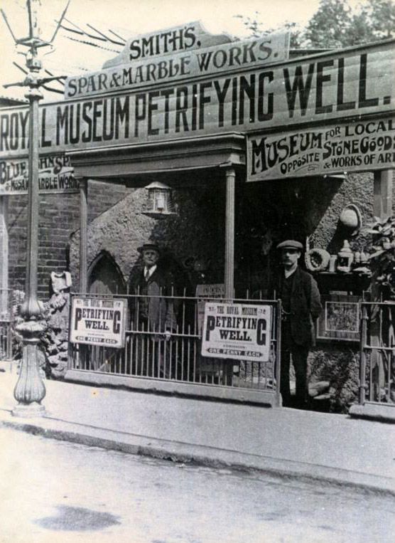 Black and white photograph showing the outside of the Petrifying Well.  There are two men standing outside