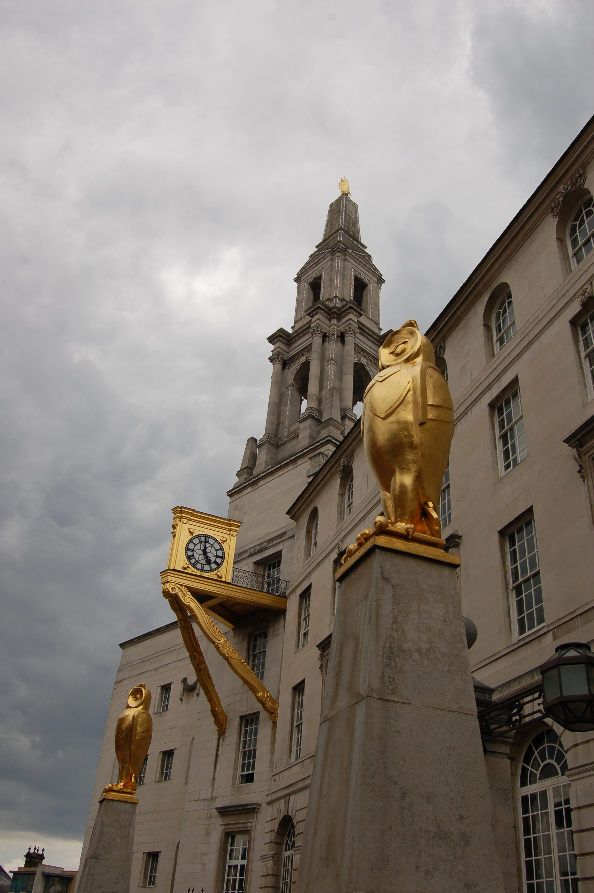 Contemporary photograph of the upper part of Leeds Civic Hall, showing two golden owls standing on plinths and the gold clock.