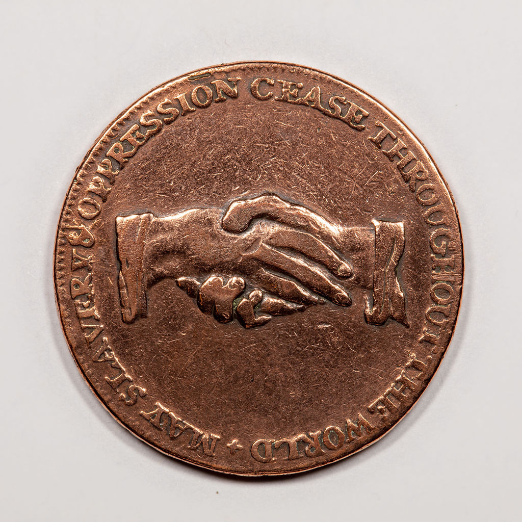 Colour photograph of a bronze coloured coin like object. It has an image of two hands in a handshake.