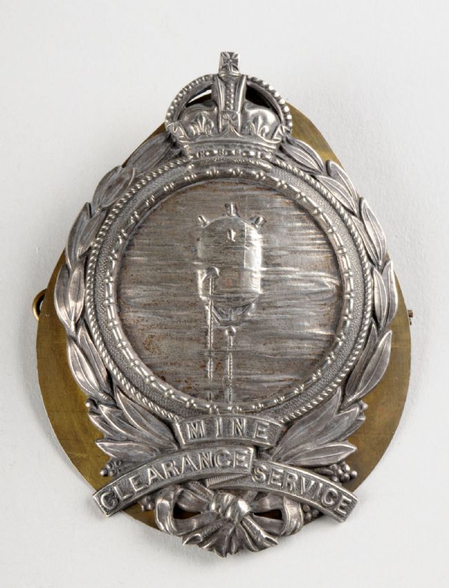 Silver coloured medal with a crown at the top and laurel wreath suround. In the centre is an image of a mine.