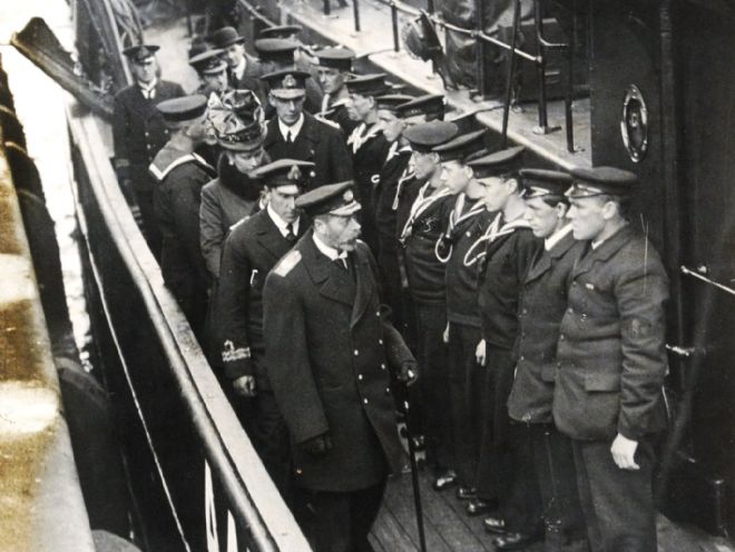 Photograph of King George V and Queen Mary with Lieutenant Commander J H Pitts inspecting a Navy trawler used for minesweeping. The sailors are lined up in uniform.