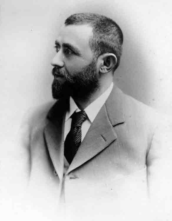 Black and white portrait photo of a bearded gentlemen wearing a suit and tie