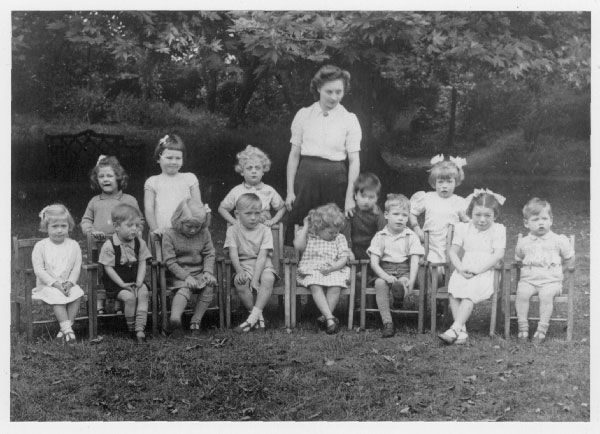 Photograph of a woman with 13 kids sitting outside.