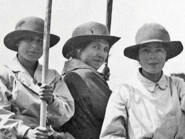 Black and white photograph of three women wearing hats with wide brims and overalls.
