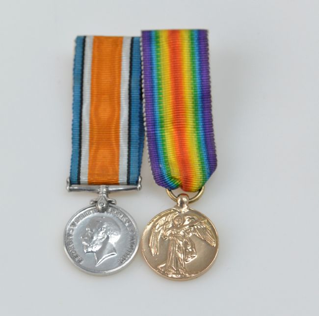 Silver coloured medal on the left with a ribbon with orange in the middle, then white, then blue.  On the right is a gold coloured medal with a rainbow ribbon.