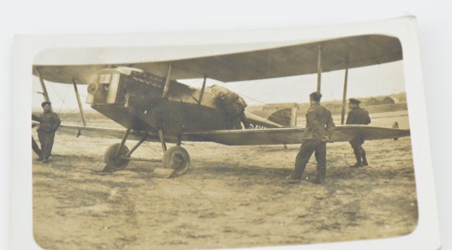 Black and white photograph of early bi-plane with three men standing near it.
