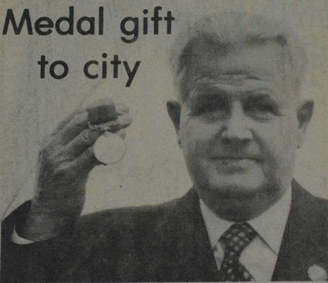 Newspaper black and white photograph of elderly man holding up a medal, with the headline 'Medal gift to city'