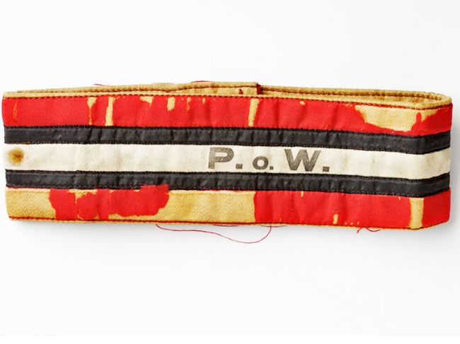 Fabric armband, originally red stripe top and bottom with two black stripes and a white stripe with 'POW' printed on.