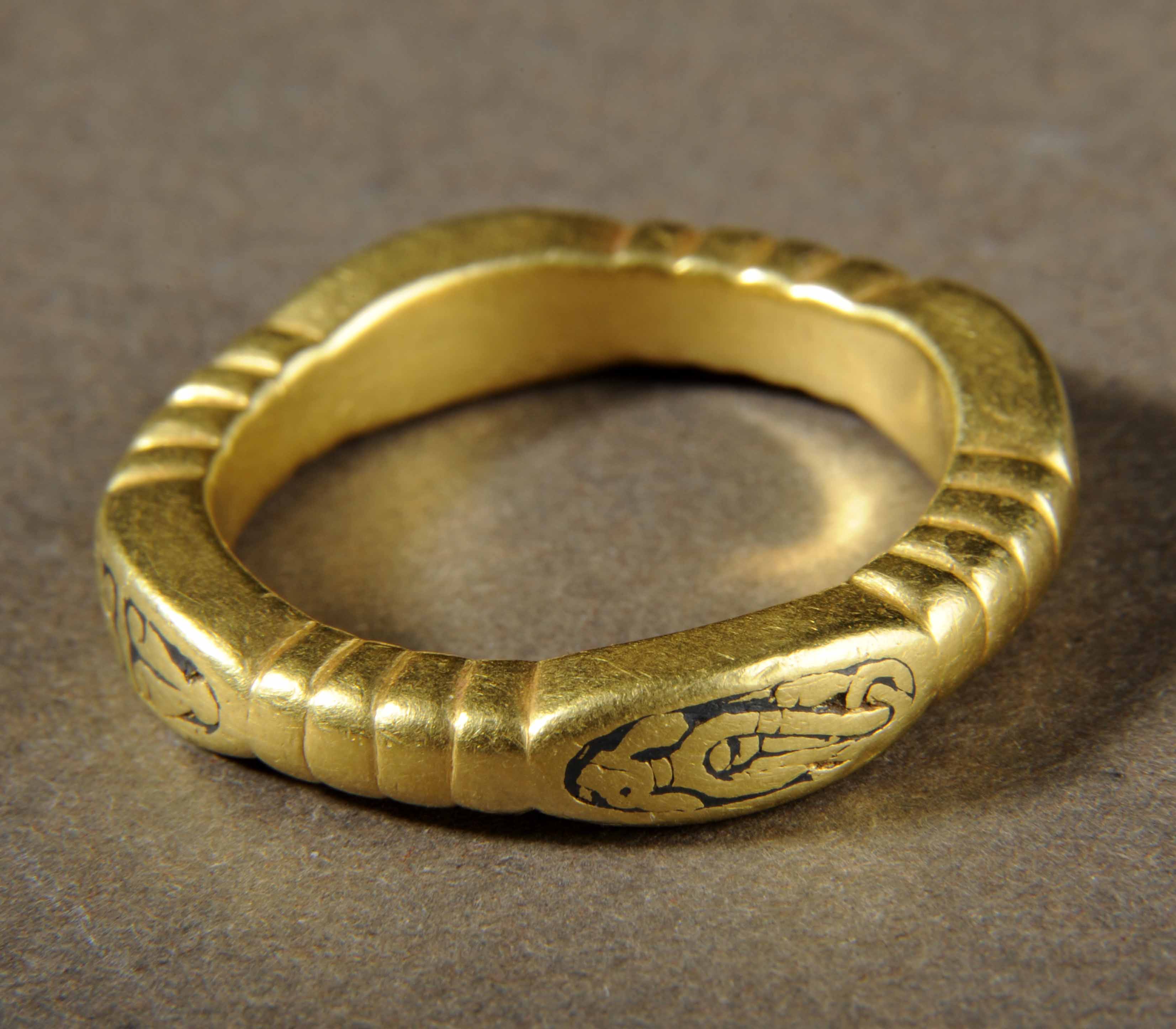 Gold ring with thick band in a rough square shape with a black design on each rounded corner.