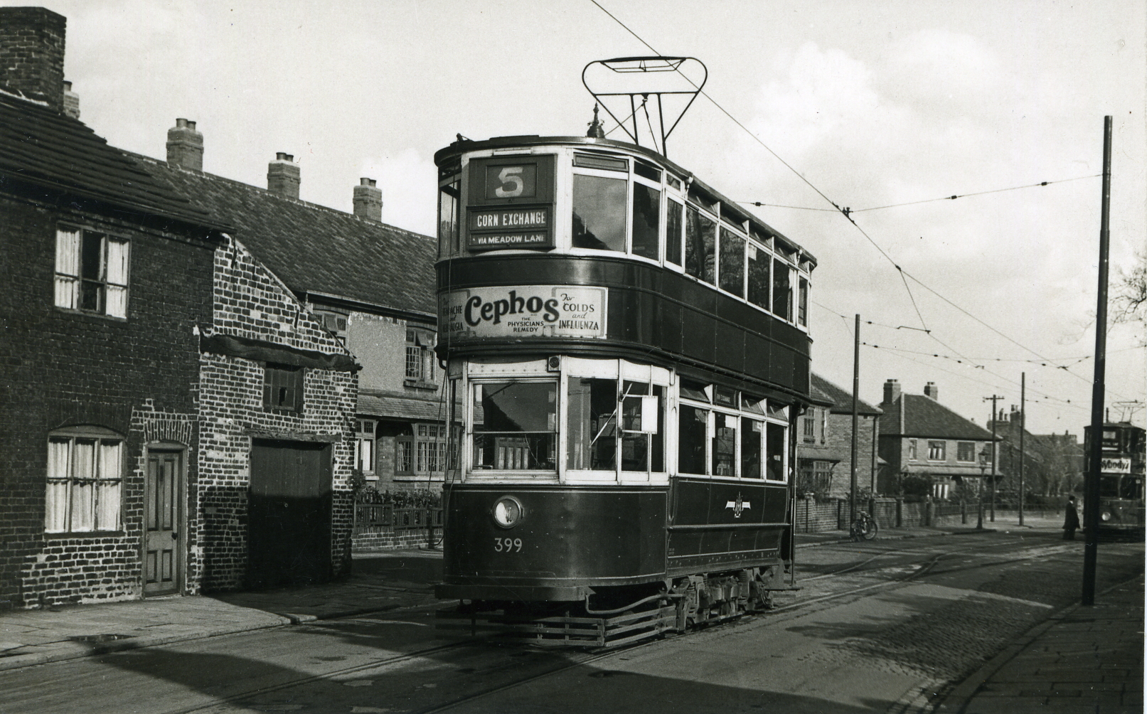A double decker tram with the number 5 on the front.  It has a round light at the front and an advert painted on the front.