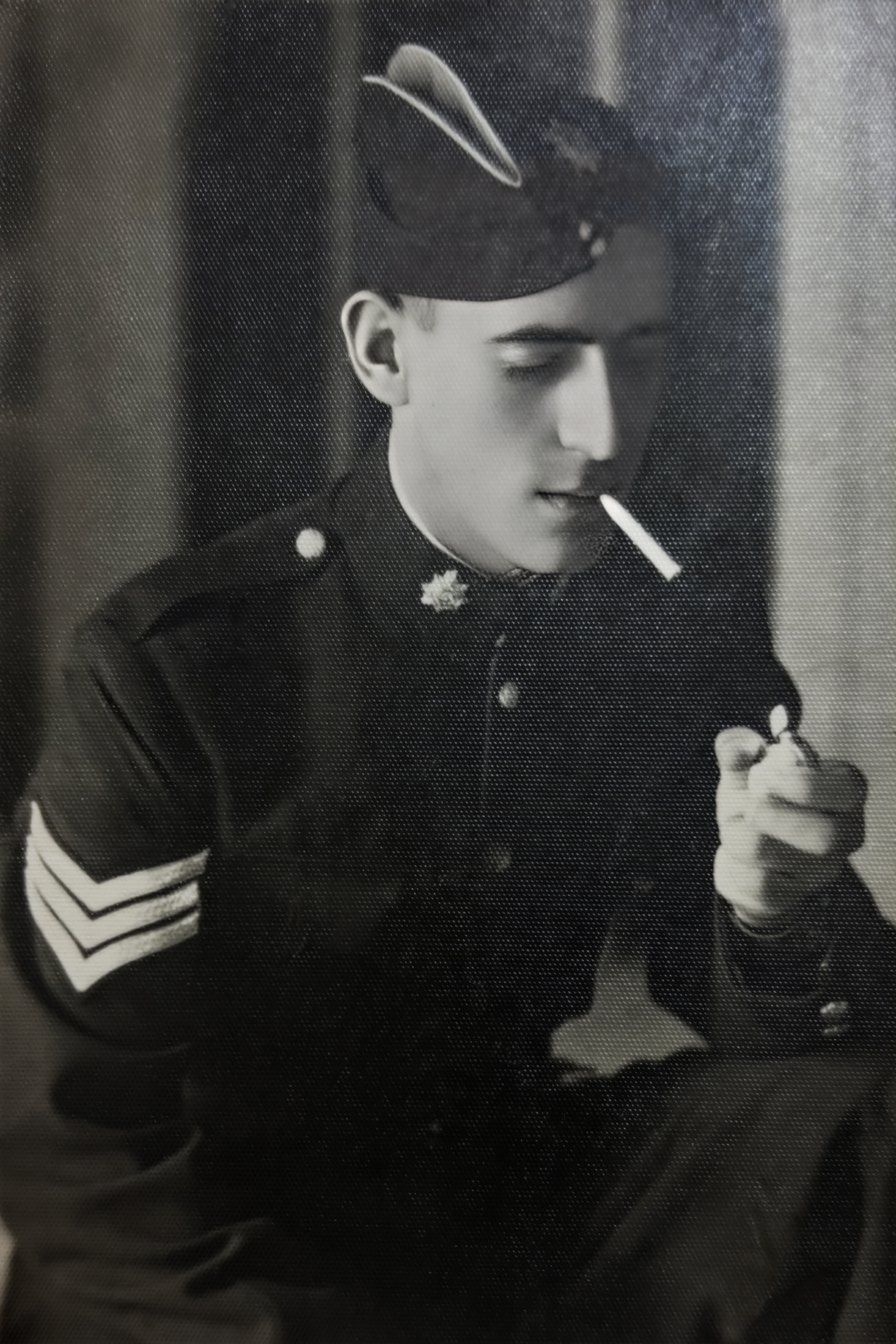 Black and white photo of a young man in military uniform lighting a cigarette.